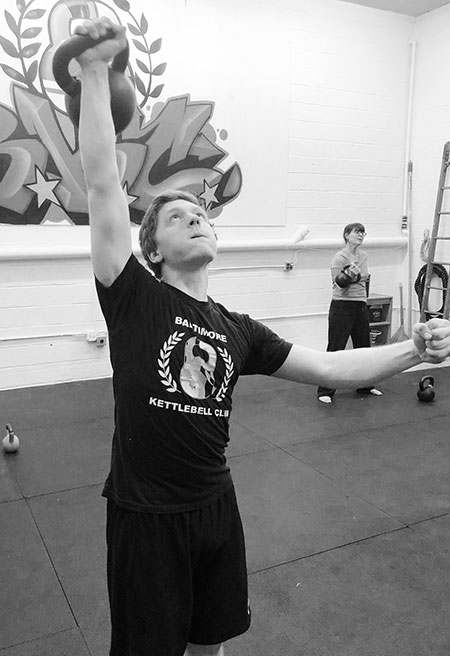 A young boy performing the one-arm kettlebell military press