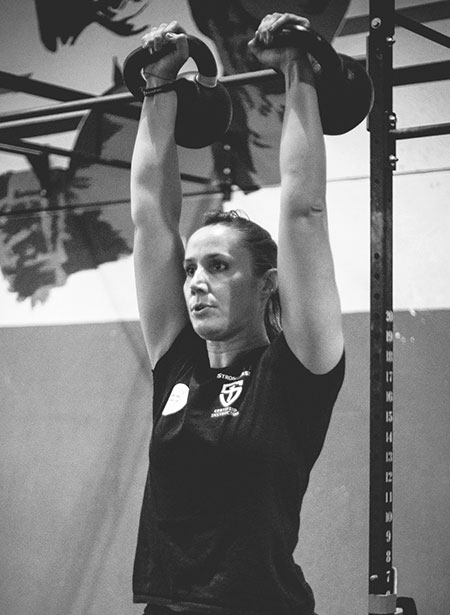 A lady performing the double kettlebell military press